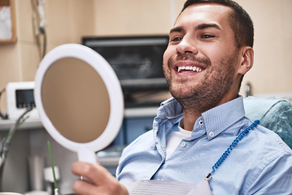 man looking at small mirror smiling | los gatos ca dentist